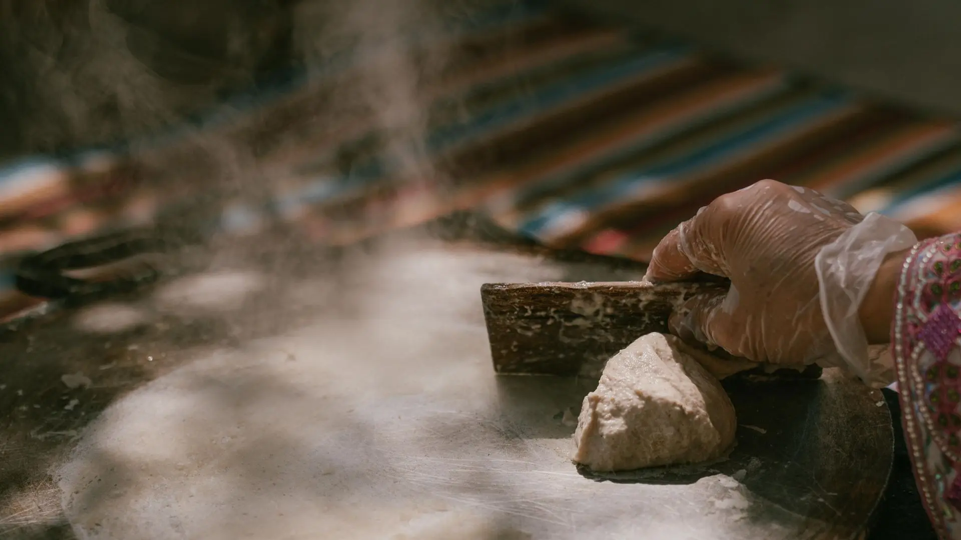Hand cooking Omani bread using wooden scraper